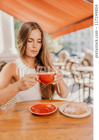 Portrait of happy woman sitting in a cafe outdoor drinking coffee. Woman while relaxing in cafe at table on street, dressed in a white T-shirt and jeans Portrait of happy woman sitting in a cafe outdoor drinking coffee. Woman while relaxing in cafe at table on street, dressed in a white T-shirt and jeans 117249804