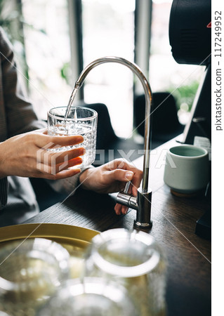 Person Filling Glass With Filtered Water at a Cafe 117249952