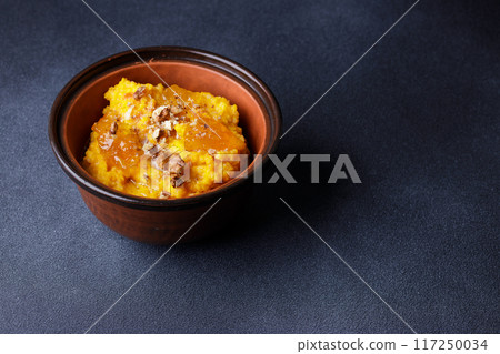 Traditional Sweet Pumpkin Porridge Served in a Clay Bowl on a Dark Background Traditional Sweet Pumpkin Porridge Served in a Clay Bowl on a Dark Background 117250034