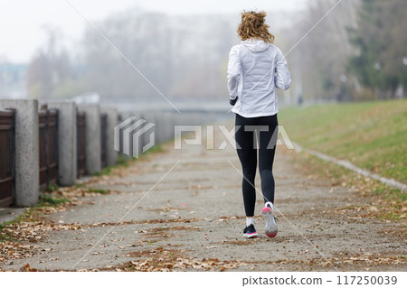 Woman Jogging along the Embankment in a Park During Foggy Autumn Morning Woman Jogging along the Embankment in a Park During Foggy Autumn Morning 117250039