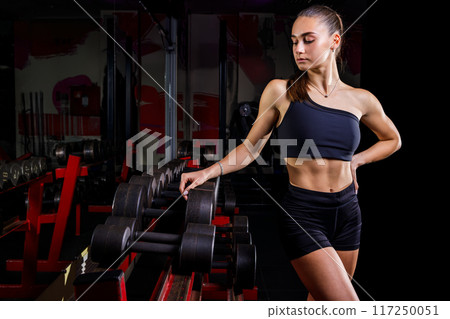 A Woman Wearing Black Sportswear Standing Near A Dumbbell Rack In The Gym 117250051