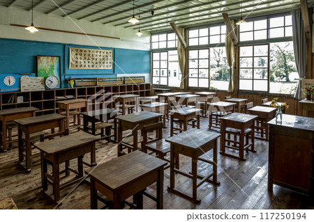 A retro classroom lit by bare light bulbs and with summer sunlight streaming in through the windows 117250194