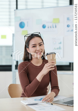 A woman is sitting at a desk with a cup in her hand A woman is sitting at a desk with a cup in her hand 117250581