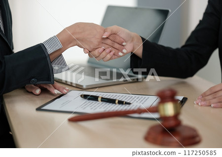 Two people shaking hands in front of a laptop and a judge's gavel 117250585