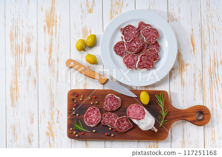 traditional Spanish salami fuet sausage or dry sausage cut in slices on a white ceramic plate, on a kitchen table, top view. traditional Spanish salami fuet sausage or dry sausage cut in slices on a white ceramic plate, on a kitchen table, top view. 117251168