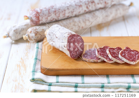 Slices of delicious spanish sausage fuet on a white wooden table. 117251169