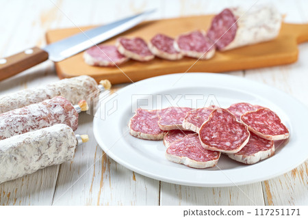 Spanish salami fuet sausage or dry sausage cut in slices on a white ceramic plate, on a kitchen table. 117251171