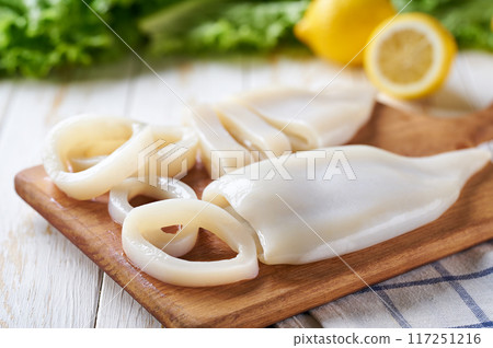Sliced rings raw squid on white wooden table with lemon and herbs.  Fresh seafood concept. 117251216