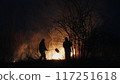Two firefighters with fire flappers extinguish a fire in the forest at night 117251618