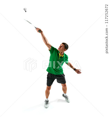 Dynamic image of concentrated young man in green sportswear, badminton player in motion with racket, preparing for match isolated on white background 117252672