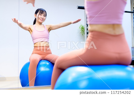 Young woman riding a balance ball in a sports gym, diet, personal gym, muscle training, women, fitness 117254202
