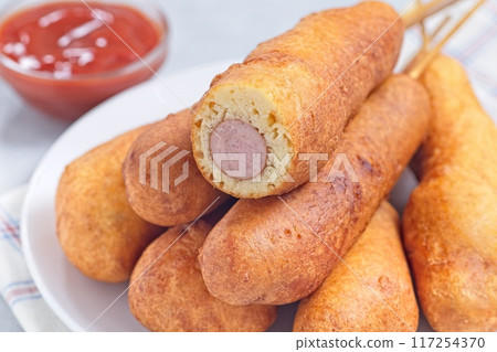 Corn dogs on white plate, served with ketchup, horizontal closeup Corn dogs on white plate, served with ketchup, horizontal closeup 117254370