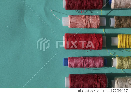 Spools of different colors are arranged in a row on a turquoise background. In the style of flat lay. 117254417