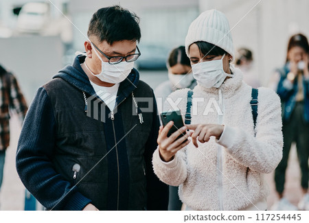 People in covid face mask and phone searching information online looking at the news on travel ban restriction on social media while stranded at the border. Modern foreign traveling people at airport 117254445
