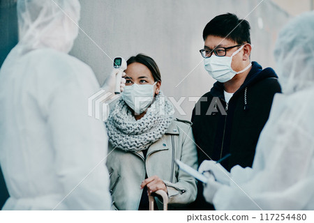 Traveling couple getting a covid temperature scan at the border with medical security doing screening test for safety during pandemic. Foreign people or traveler arriving at an airport with face mask Traveling couple getting a covid temperature scan at the border with medical security doing screening test for safety during pandemic. Foreign people or traveler arriving at an airport with face mask 117254480