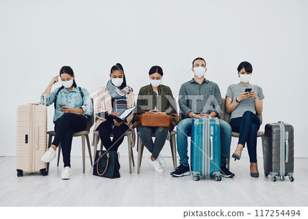 Travel and tourism during the pandemic with passengers wearing masks and being safe in an airport waiting line. Group of people in a departure lounge, ready to board and complying with covid protocol 117254494