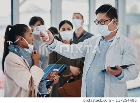 A travel healthcare worker testing covid temperature at the airport using an infrared thermometer. Medical professional doing a coronavirus check on a woman at an entrance to prevent the spread 117254496