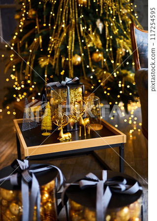 Luxurious interior of the room for Christmas and New Year. Living room in gray and gold tones with a sofa, many gifts, golden balls, ice lights, two Christmas trees 117254595
