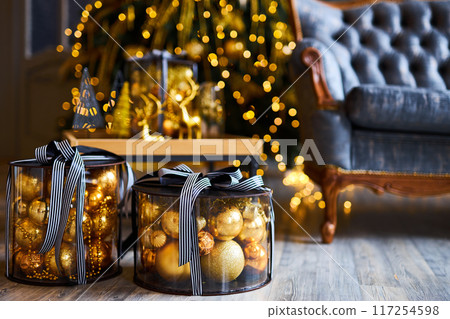 Luxurious interior of the room for Christmas and New Year. Living room in gray and gold tones with a sofa, many gifts, golden balls, ice lights, two Christmas trees 117254598