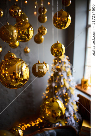 Luxurious interior of the room for Christmas and New Year. Living room in gray and gold tones with a sofa, many gifts, golden balls, ice lights, two Christmas trees Luxurious interior of the room for Christmas and New Year. Living room in gray and gold tones with a sofa, many gifts, golden balls, ice lights, two Christmas trees 117254600