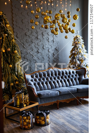 Luxurious interior of the room for Christmas and New Year. Living room in gray and gold tones with a sofa, many gifts, golden balls, ice lights, two Christmas trees 117254607