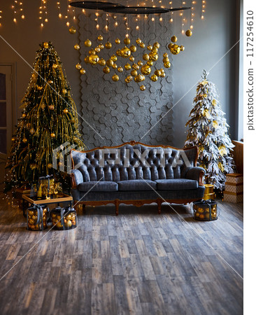 Luxurious interior of the room for Christmas and New Year. Living room in gray and gold tones with a sofa, many gifts, golden balls, ice lights, two Christmas trees Luxurious interior of the room for Christmas and New Year. Living room in gray and gold tones with a sofa, many gifts, golden balls, ice lights, two Christmas trees 117254610