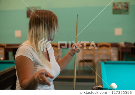 Copy space. A beautiful woman holding a billiard cue in her hands looks to the side, thinking about the next shot. A woman enjoys playing billiards in her free time. 117255596
