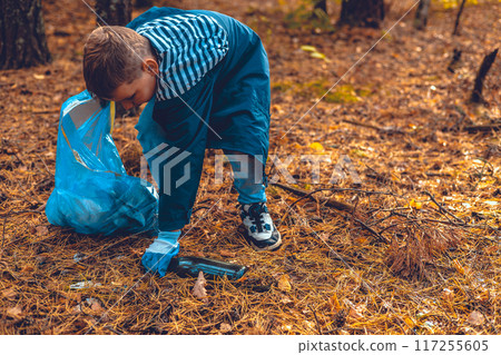 Cleaning the forest from garbage waste. A child with a garbage bag collects garbage in the forest. The problem of forest pollution with waste, an environmental disaster. 117255605