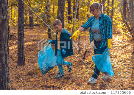 Eco activists mother and son walk through the forest with bags and collect garbage. Mom teaches her baby to take care of nature and save it from pollution by paste waste. 117255606