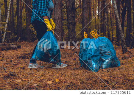 A woman volunteer puts together bags of garbage collected from the forest. A woman has collected a lot of household waste in garbage bags in the forest and is preparing it for removal. Ecology. A woman volunteer puts together bags of garbage collected from the forest. A woman has collected a lot of household waste in garbage bags in the forest and is preparing it for removal. Ecology. 117255611