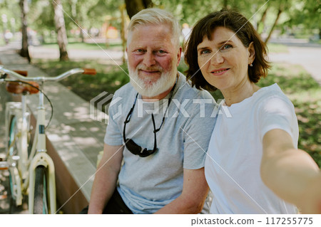 Senior brunette woman taking selfie with her beloved silver-haired husband while they having walk 117255775