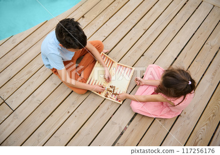 Children playing backgammon on a wooden deck by the poolside on a summer day 117256176