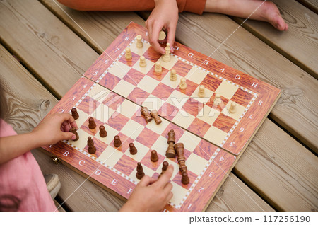 Children playing chess on a wooden deck, showing strategy and intellectual engagement 117256190