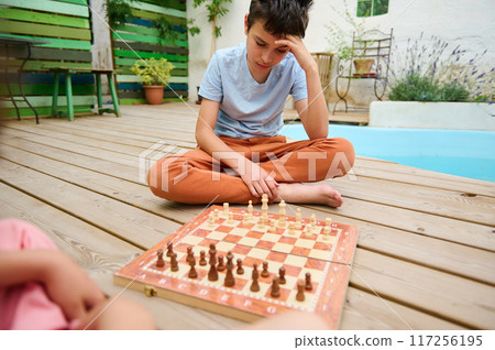 Boy playing chess outdoors while thinking about his next move Boy playing chess outdoors while thinking about his next move 117256195