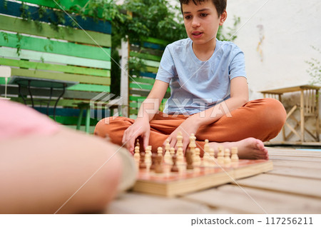 Young boy concentrating on a game of chess in a colorful outdoor setting Young boy concentrating on a game of chess in a colorful outdoor setting 117256211