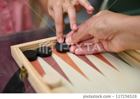 Close-up of a parent and child playing a game of backgammon together Close-up of a parent and child playing a game of backgammon together 117256528
