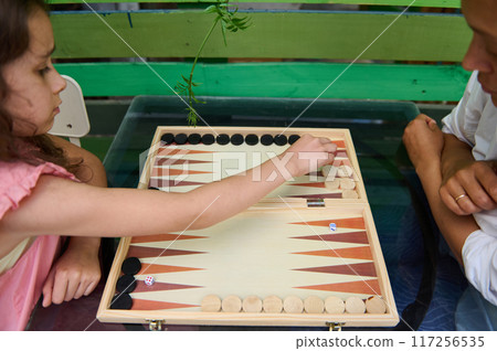 Child playing backgammon with adult, enjoying quality family time outdoors Child playing backgammon with adult, enjoying quality family time outdoors 117256535
