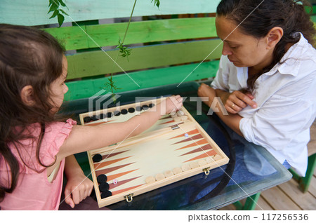 Mother and daughter bonding over a game of backgammon outdoors on a sunny day Mother and daughter bonding over a game of backgammon outdoors on a sunny day 117256536