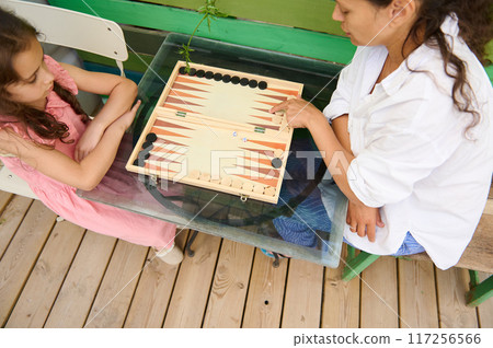 Mother and daughter playing backgammon at home on a wooden table 117256566