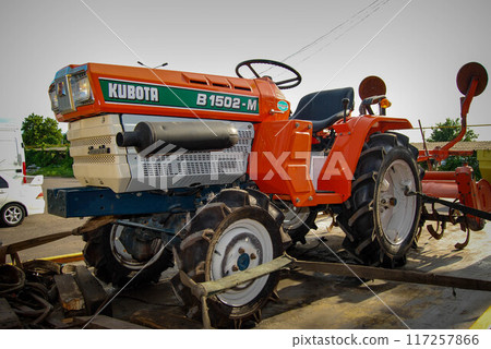 Small, multi-purpose tractor on a tow truck.An orange tractor attached to the platform of a recovery vehicle. 117257866