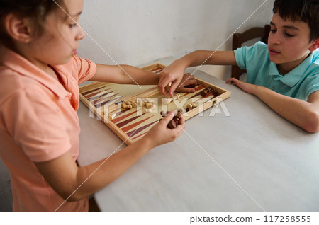 Children playing backgammon together at home on a wooden board game Children playing backgammon together at home on a wooden board game 117258555