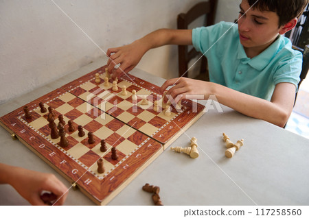 Young boy playing chess on a wooden chessboard with focus on hand and chess pieces Young boy playing chess on a wooden chessboard with focus on hand and chess pieces 117258560