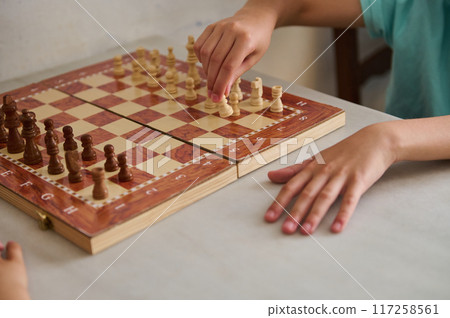 Close-up of children's hands playing a chess game on a wooden chessboard 117258561
