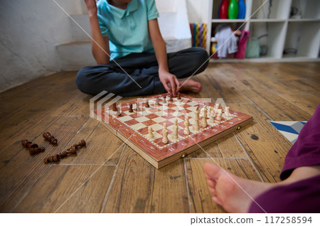 Children playing an intense game of chess on a wooden board in a cozy home setting 117258594
