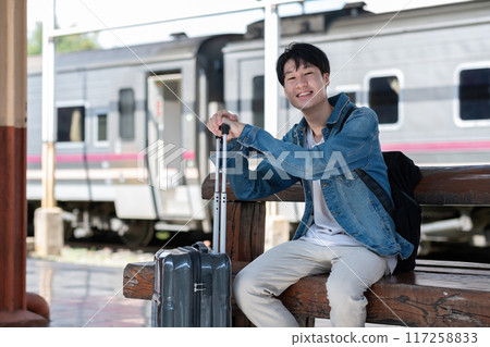 A young man holding a suitcase waits for a train at the train station for traveling. A young man holding a suitcase waits for a train at the train station for traveling. 117258833