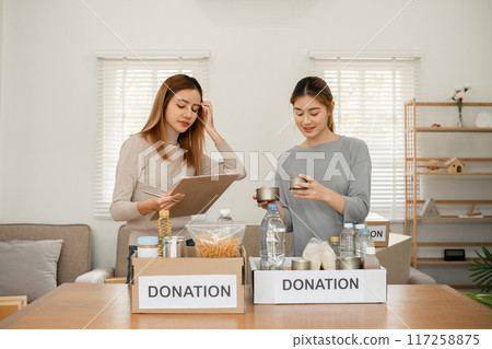 Two young female volunteers help pack food into donation boxes and prepare donation boxes to take to charities. Two young female volunteers help pack food into donation boxes and prepare donation boxes to take to charities. 117258875
