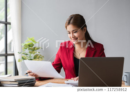 Beautiful accountant sitting working with laptop calculating financial and tax figures for company on desk in living room. Beautiful accountant sitting working with laptop calculating financial and tax figures for company on desk in living room. 117258912