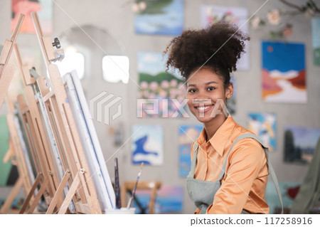 A young black artist paints acrylic paints on canvas with determination in her painting studio A young black artist paints acrylic paints on canvas with determination in her painting studio 117258916