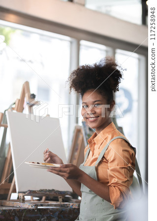 A young black artist paints acrylic paints on canvas with determination in her painting studio A young black artist paints acrylic paints on canvas with determination in her painting studio 117258948
