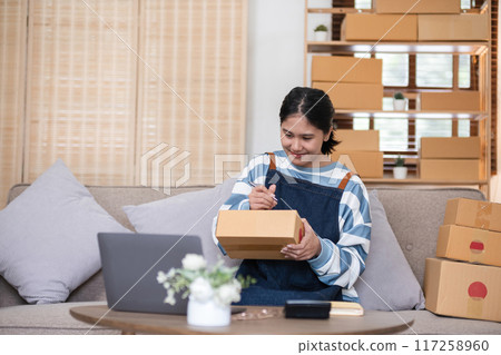 entrepreneurs small business Write shipping information on a cardboard box in home office. Small business operators preparing to ship to customer 117258960